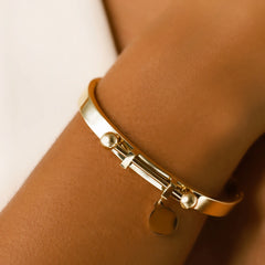 Model wearing the Coins Bangle, a gold bangle bracelet with a unique toggle closure and a dangling coin charm. ||| GOLD