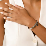 Model wearing the Coins Bangle, a silver bangle bracelet with a unique toggle closure and a dangling coin charm. ||| SILVER