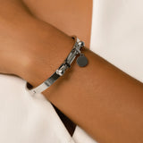 Model wearing the Coins Bangle, a silver bangle bracelet with a unique toggle closure and a dangling coin charm. ||| SILVER