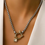 The Herradura Lock Single Necklace, a bold silver chain necklace featuring a statement gold clasp and lock pendant. This mixed-metal piece combines modern elegance with an edgy touch, perfect for adding sophistication to any outfit.