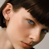 Model wearing the Ear Cuff with Chain Earring which features a hoop cuff with shimmering diamonds and a dainty chain connected to a pear-shaped diamond earring.