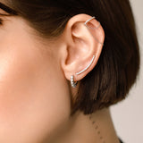 Model wearing the Dancing Ear Cuff, a silver ear cuff featuring delicate cascading chains and shimmering diamond accents and also two more earrings with diamonds.