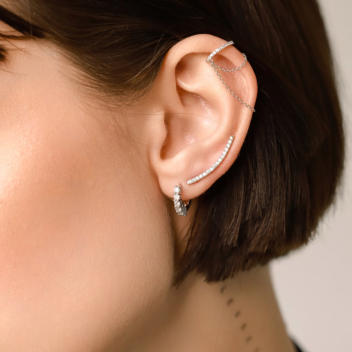 Model wearing the Dancing Ear Cuff, a silver ear cuff featuring delicate cascading chains and shimmering diamond accents and also two more earrings with diamonds.