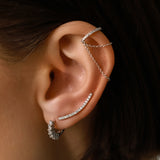 Model wearing the Dancing Ear Cuff, a silver ear cuff featuring delicate cascading chains and shimmering diamond accents and also two more earrings with diamonds.