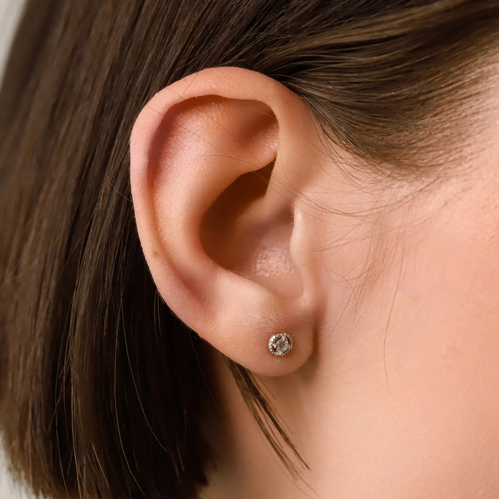 The SINGLE MINI STUD EARRING, which is a minimalist silver earring featuring a single sparkling center stone surrounded by a delicate circular design, ideal for a subtle and elegant everyday accessory.