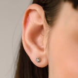 The SINGLE MINI STUD EARRING, which is a minimalist silver earring featuring a single sparkling center stone surrounded by a delicate circular design, ideal for a subtle and elegant everyday accessory.