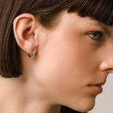 The Prong Hoops, which are a pair of silver hoop earrings, feature a stunning row of sparkling prong-set cubic zirconia stones along the front for a dazzling effect. These elegant hoops are perfect for adding a touch of glamour to any outfit, making them versatile for both everyday wear and special occasions ||| SILVER
