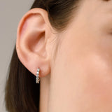 The Prong Hoops, which are a pair of silver hoop earrings, feature a stunning row of sparkling prong-set cubic zirconia stones along the front for a dazzling effect. These elegant hoops are perfect for adding a touch of glamour to any outfit, making them versatile for both everyday wear and special occasions ||| SILVER