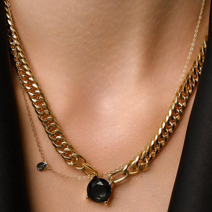 Model wearing The Emerald Dot Necklace Set, a two-piece gold necklace featuring a delicate chain with a single emerald pendant and a matching choker chain.