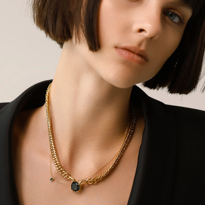 Model wearing the Emerald Dot Necklace Set, a two-piece gold necklace featuring a delicate chain with a single emerald pendant and a matching choker chain.