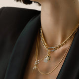 Model wearing the Just Click Tag Necklace Set, a four-piece gold necklace set featuring a Cuban link chain, a box chain, and a rope chain with diamond-like accents, two dog tag charms, and a spike charm.