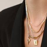 The Letter Necklace Set, which is a three-piece layered necklace set, features a mix of gold and silver chains for a bold and versatile look. It includes a gold square charm engraved with the letter 'X' and a sleek lightning bolt pendant, adding unique detail to the layered design.