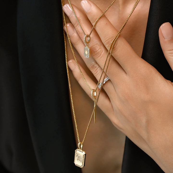 Model wearing the You and the Needle Necklace Set, a three-piece gold necklace set with a needle pendant and initial charm.