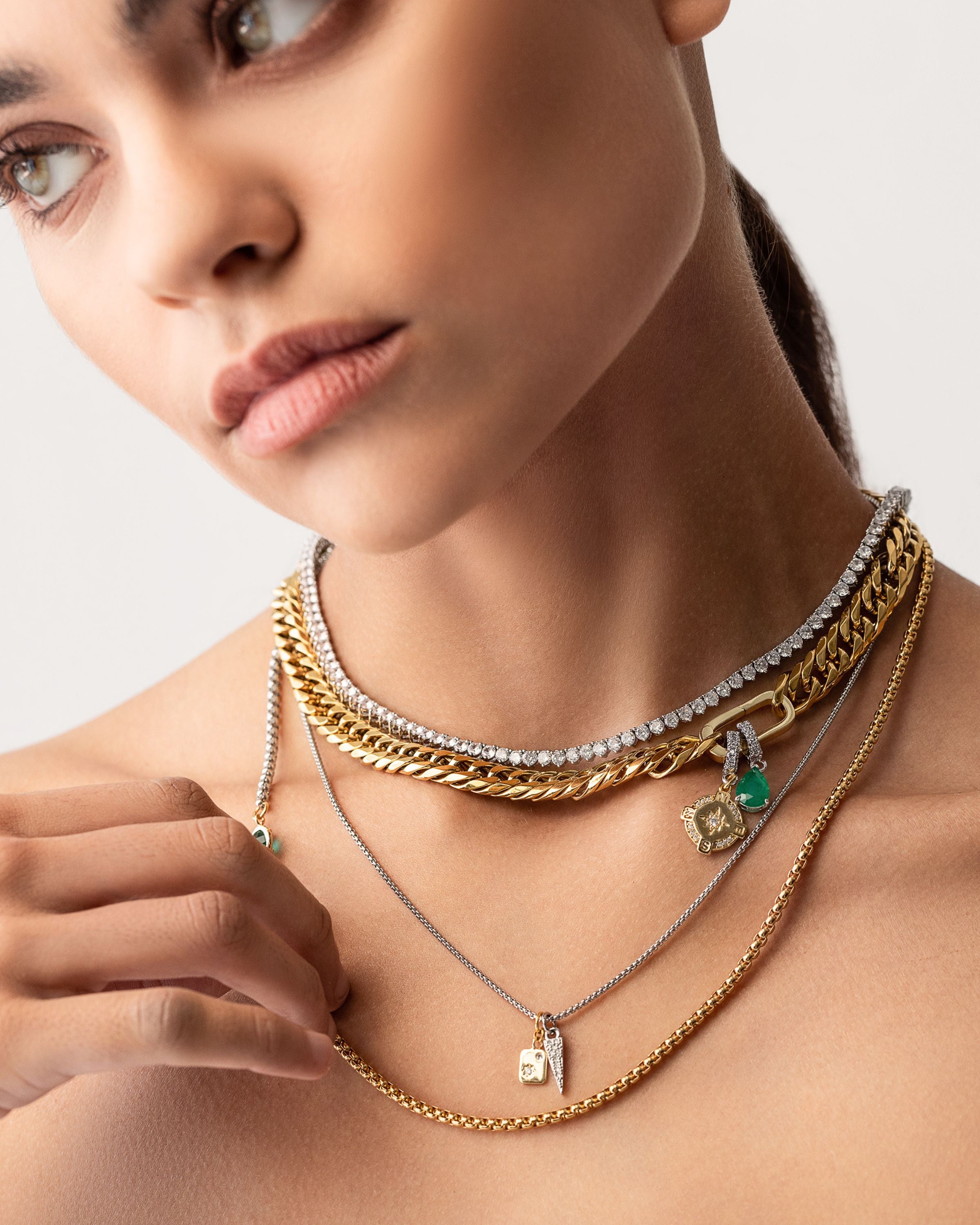 Model wearing the Just Click Emerald Tennis Necklace Set, a four-piece gold and silver necklace set featuring a variety of chains with diamond-like accents, emerald accents, and a variety of charms