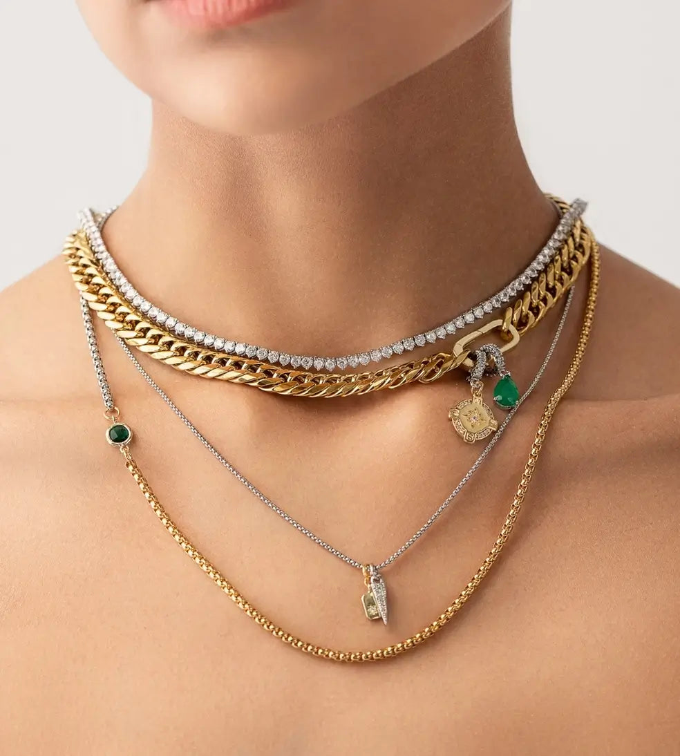 Layered gold and silver necklaces with emerald accents styled on a woman’s neck, showcasing modern luxury jewelry.