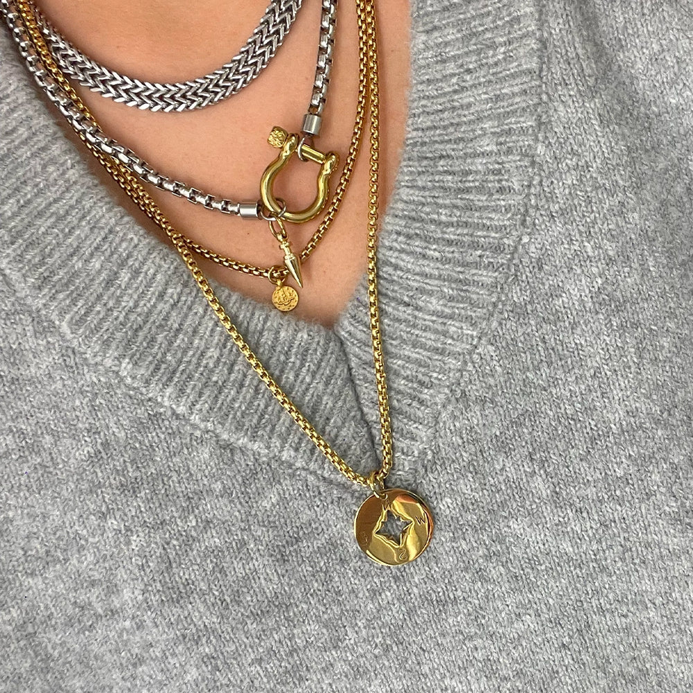 Multiple layered gold and silver necklaces featuring unique charms, styled elegantly over a cozy gray sweater.