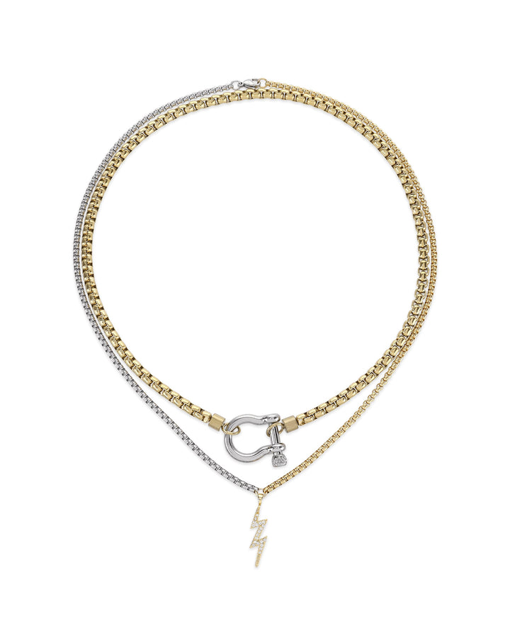 The Herradura Thunder Layered Necklace, a two-piece silver and gold necklace set featuring a box chain and a Cuban chain with a gold horseshoe clasp and a lightning bolt charm accented with diamond-like stones.