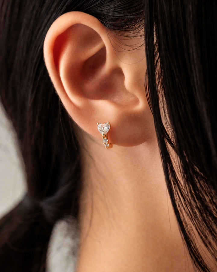 gold-tone huggie earring highlighted by a prominent heart-shaped cubic zirconia stone 