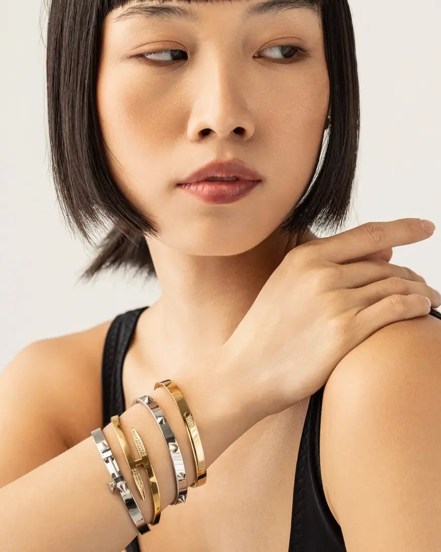 "Model wearing a stack of gold and silver bangles, including textured and smooth cuffs, styled with a black tank top for a modern minimalist look."