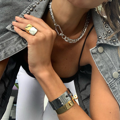 Close-up of a hand wearing chunky rings and layered bracelets, paired with a silver chain necklace and a stylish denim jacket.