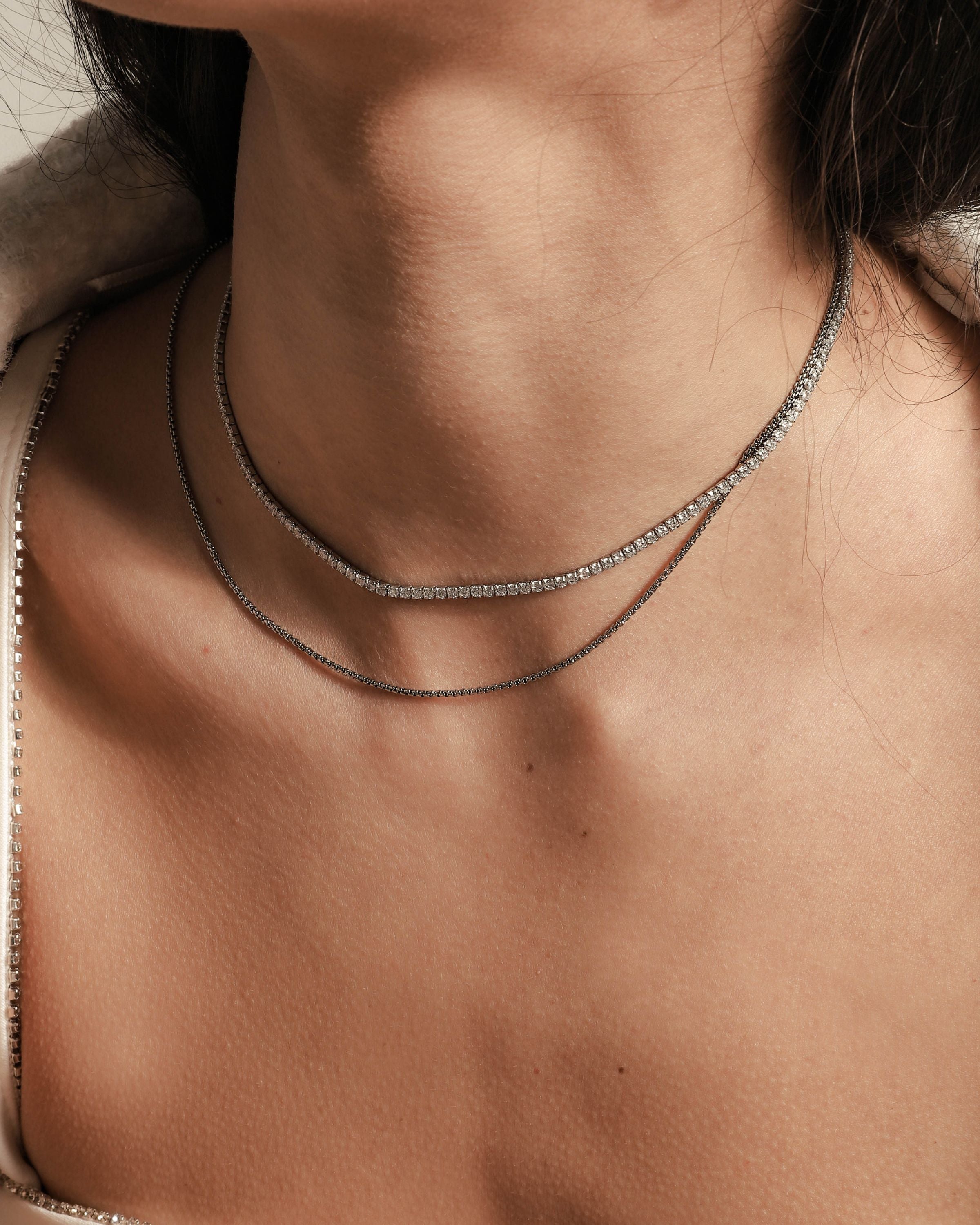 Model wearing the TENNIS DAINTY NECKLACE SET which includes 14" and 16" necklaces.  One is Stainless steel Rhodium plated chain, 1mm Wide and the shorter one is a Rhodium-plated brass/cubic zirconia tennis necklace, 2 mm wide.