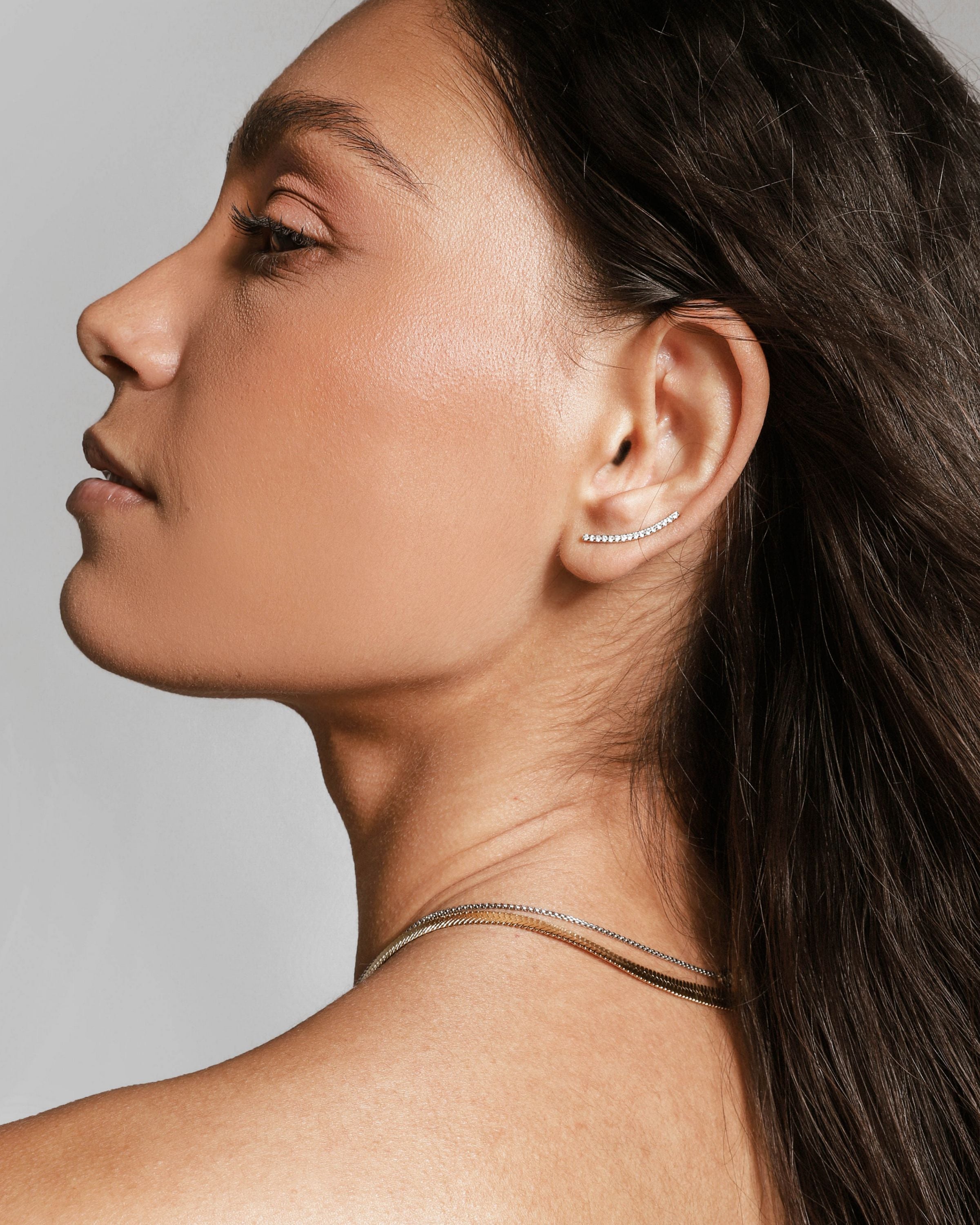 Model wearing one of the ear set which is a long arch earring filled surrounded with encrusted zirconia.