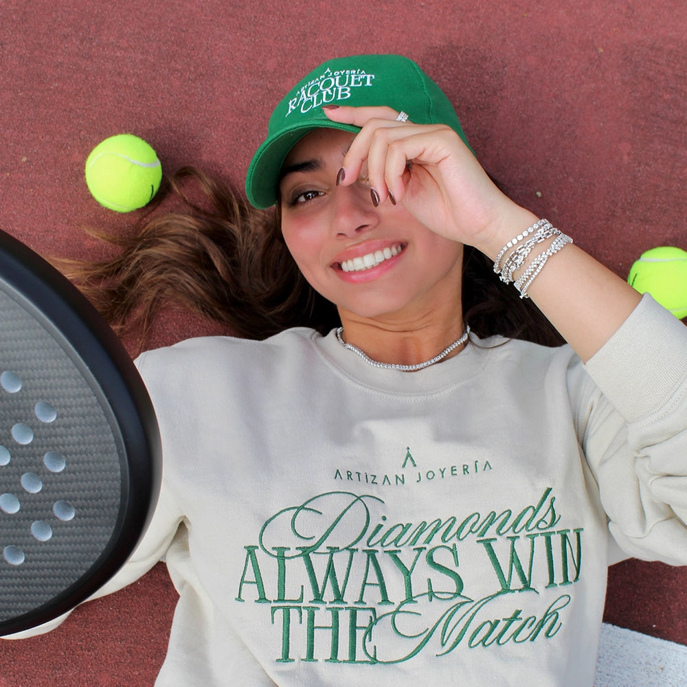 A playful photo of a woman on a tennis court, smiling while wearing a sweatshirt with 