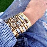 Wrist stacked with multiple bracelets, including the Coin Bangle and Herradura Bangle in mixed gold and silver metal, styled with a casual denim and striped shirt outfit. ||| MIX SILVER