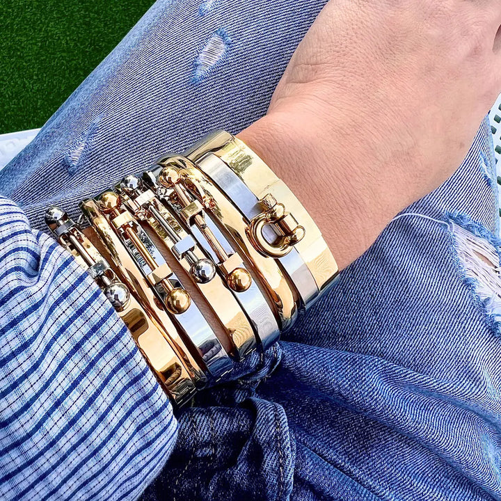 Wrist stacked with multiple bracelets, including the Coin Bangle and Herradura Bangle in mixed gold and silver metal, styled with a casual denim and striped shirt outfit. ||| MIX SILVER