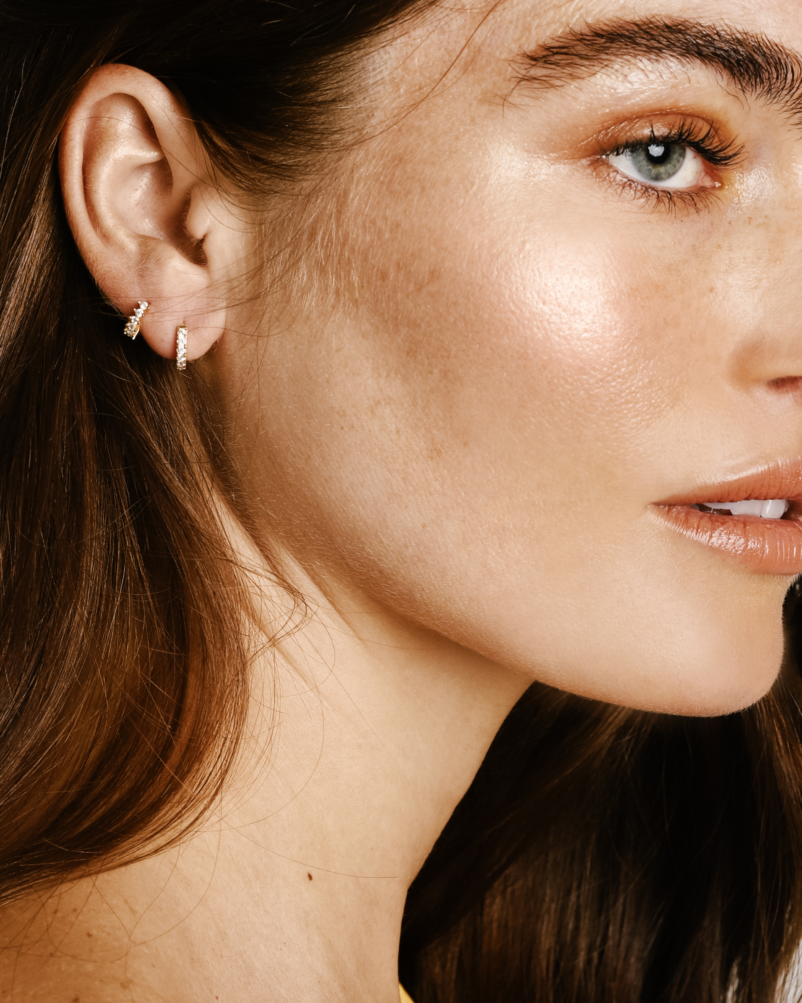 Model wearing the TINY HUGGIES which is made of 18K gold plated huggies earring covered in Cubic zirconia and has an outer diameter size of 0.9 mm.||| GOLD/8mm