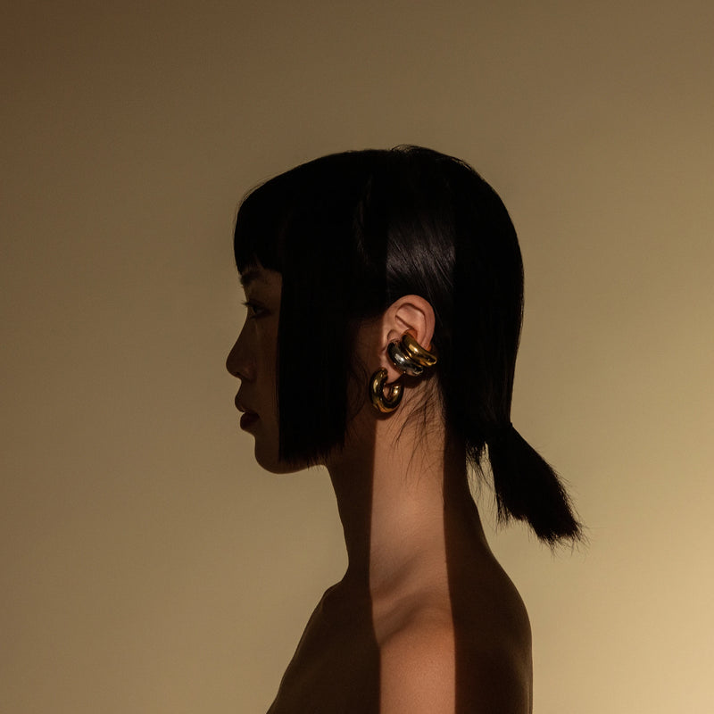 Model wearing three Chunky Bagel Ear Cuffs,  gold and silver ear cuffs with a thick, rounded design.