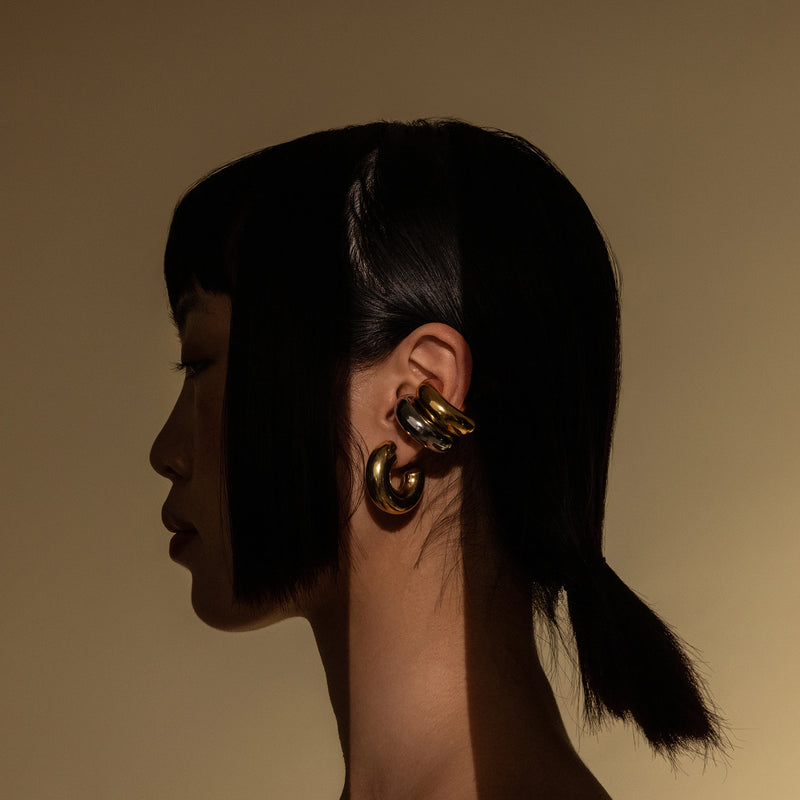 Model wearing three Chunky Bagel Ear Cuffs,  gold and silver ear cuffs with a thick, rounded design.