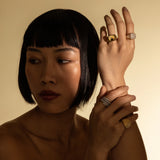 Model wearing the Honeycomb Pinky Pave Ring, a gold ring with a  geometric design featuring pave-set diamond-like stones and three other artizan rings.