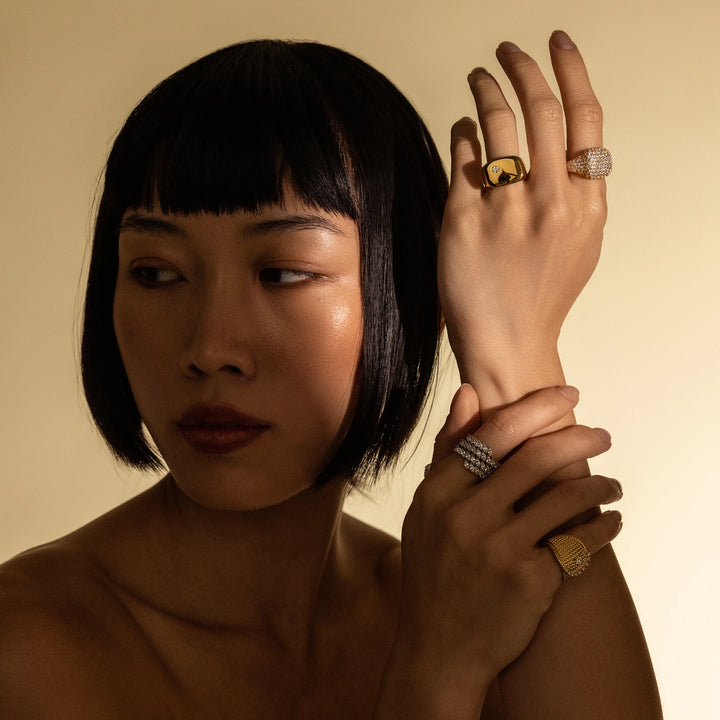 Model wearing the Honeycomb Pinky Pave Ring, a gold ring with a  geometric design featuring pave-set diamond-like stones and three other artizan rings.