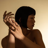 Model wearing the Honeycomb Pinky Pave Ring, a gold ring with a  geometric design featuring pave-set diamond-like stones and three other artizan rings.