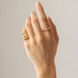 The Abuela Ring worn on the pinky finger which is a Gold textured statement ring with diamond accents in a unique wave design.