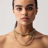 Model wearing The Just Click Emerald Tennis Necklace Set, a four-piece gold and silver necklace set featuring a variety of chains with diamond-like accents, emerald accents, and a variety of charms.