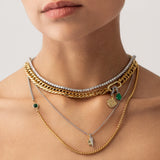 Model wearing The Just Click Emerald Tennis Necklace Set, a four-piece gold and silver necklace set featuring a variety of chains with diamond-like accents, emerald accents, and a variety of charms.