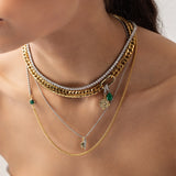 Model wearing the Just Click Emerald Tennis Necklace Set, a four-piece gold and silver necklace set featuring a variety of chains with diamond-like accents, emerald accents, and a variety of charms.