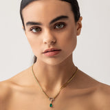 Model wearing a gold necklace with can opener clasp with the Emerald Teardrop Clip On Charm, a gold charm featuring a single teardrop-shaped emerald. ||| GOLD
