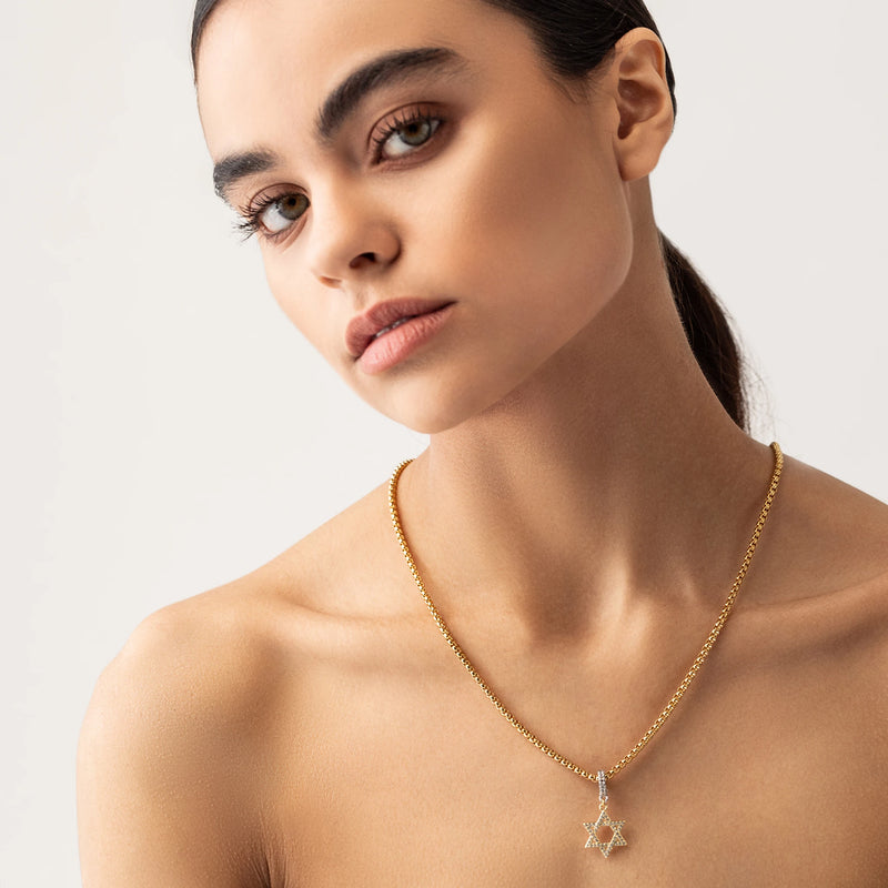 Model wearing a gold necklace with The Gold David’s Star Charm  which is a Six-Pointed Star-Shaped Gold Charm with Diamond Accents.