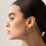Model wearing the SLIM BAGEL HOOPS which is a pair of gold bagel inspired hoops.