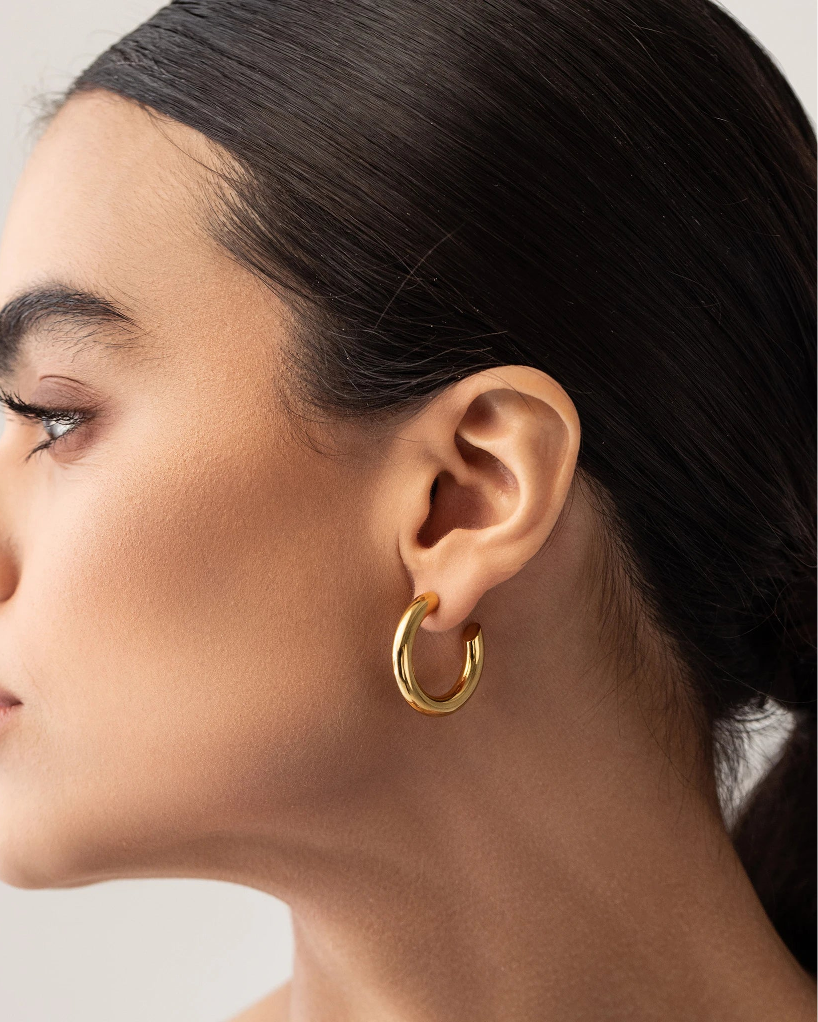 Model wearing the SLIM BAGEL HOOPS which is a pair of gold bagel inspired hoops.