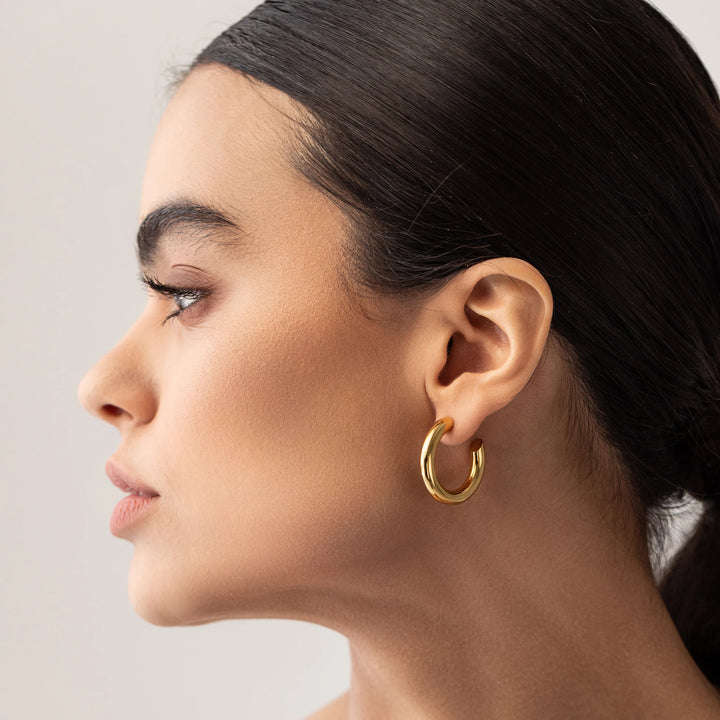 Model wearing the SLIM BAGEL HOOPS which is a pair of gold bagel inspired hoops.