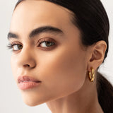 Model wearing the SLIM BAGEL HOOPS which is a pair of gold bagel inspired hoops.