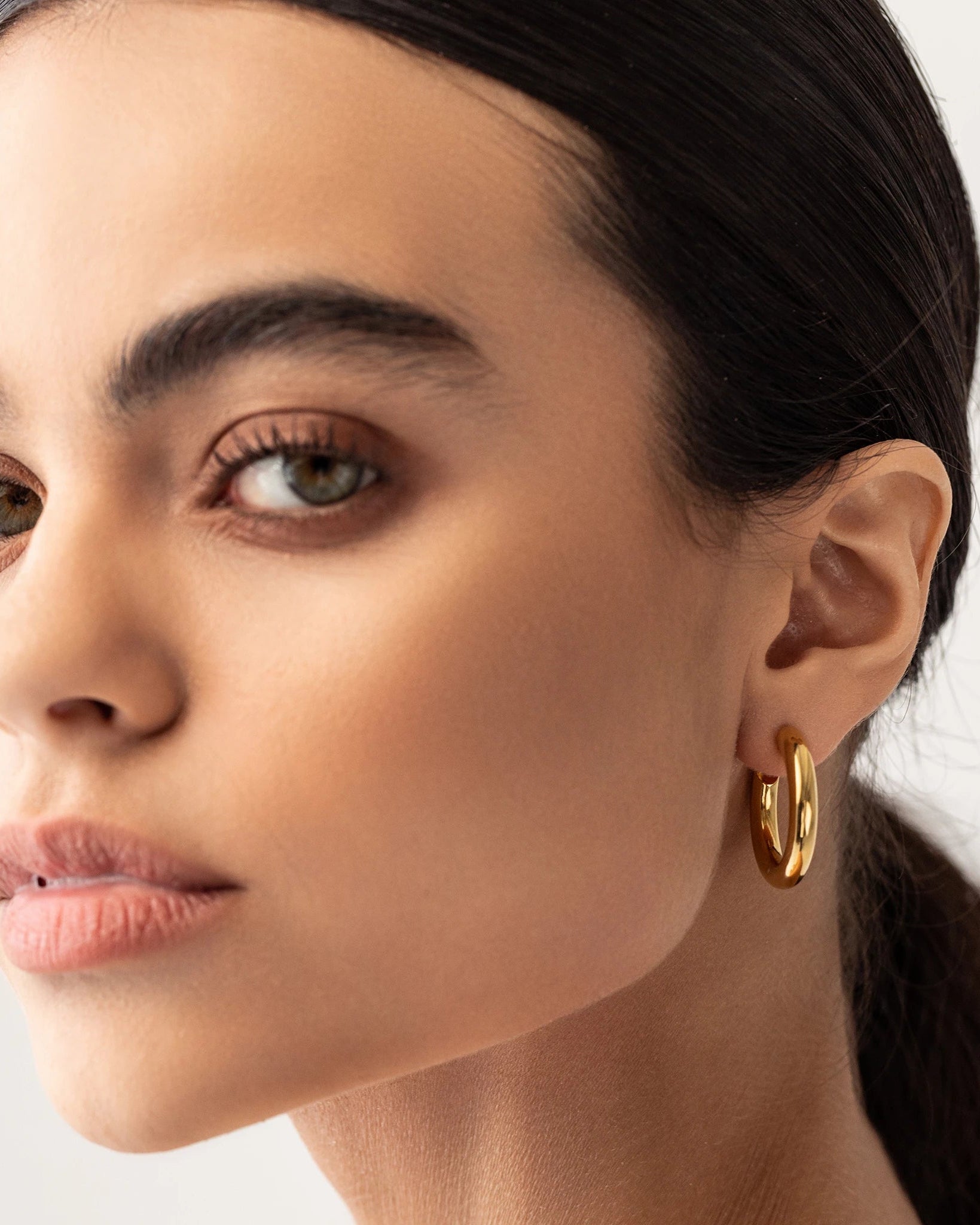 Model wearing the SLIM BAGEL HOOPS which is a pair of gold bagel inspired hoops.