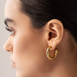 The Slim Bagel Hoops, which are a pair of elegant gold hoop earrings featuring a polished, chunky design, offering a bold yet refined statement for any occasion.