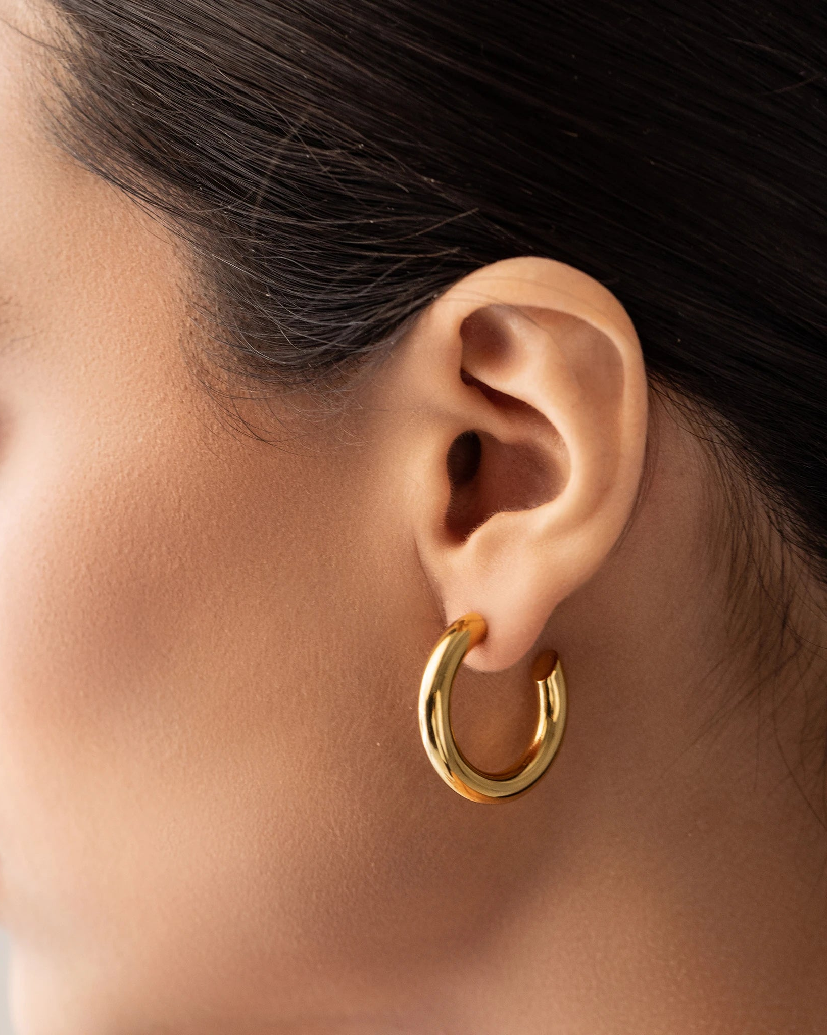 The Slim Bagel Hoops, which are a pair of elegant gold hoop earrings featuring a polished, chunky design, offering a bold yet refined statement for any occasion.