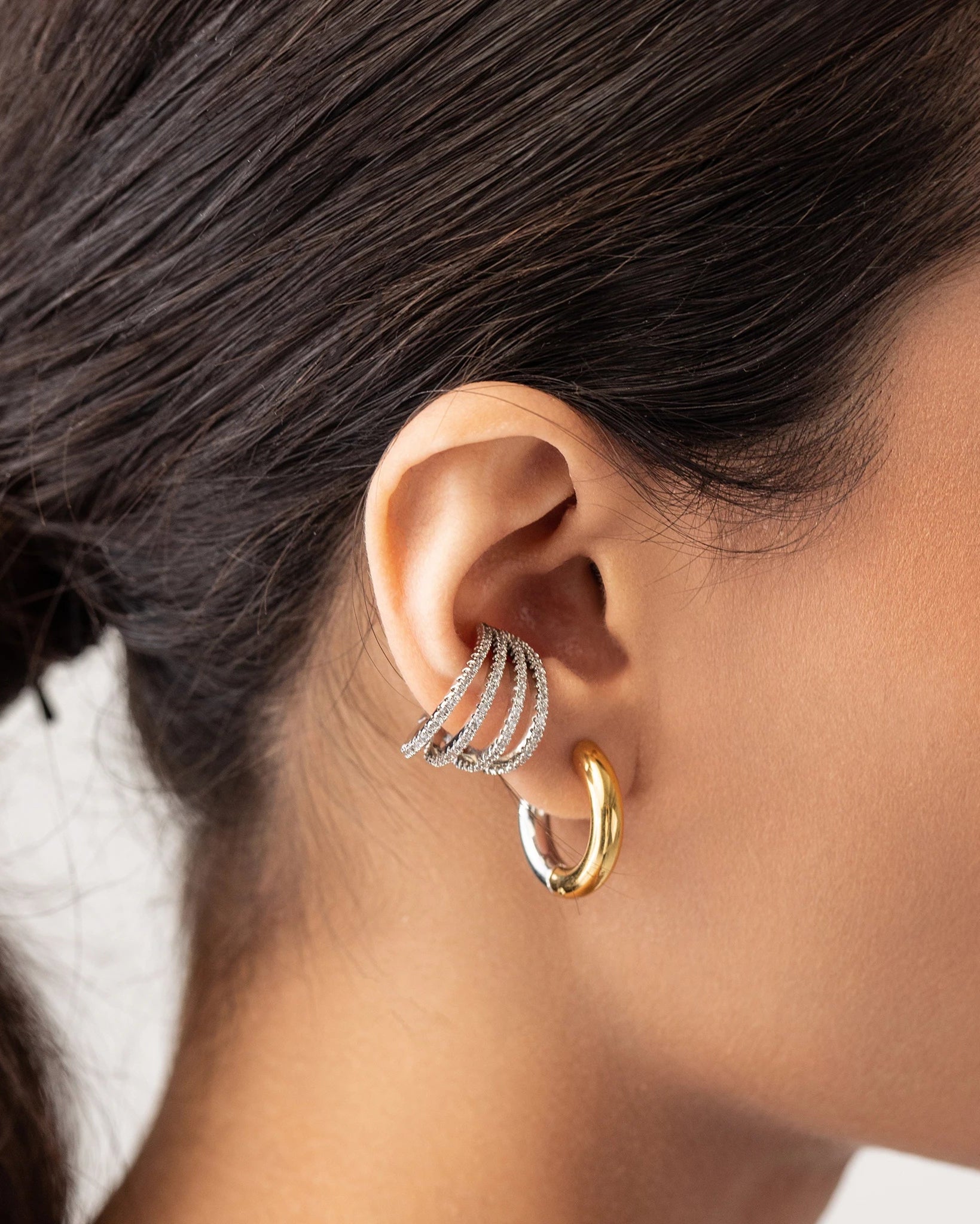 Model wearing the Slim Mix Huggies, a chic pair of two-tone hoop earrings features a combination of gold and silver tones and also a 4 hoop design diamond filled ear cuff.