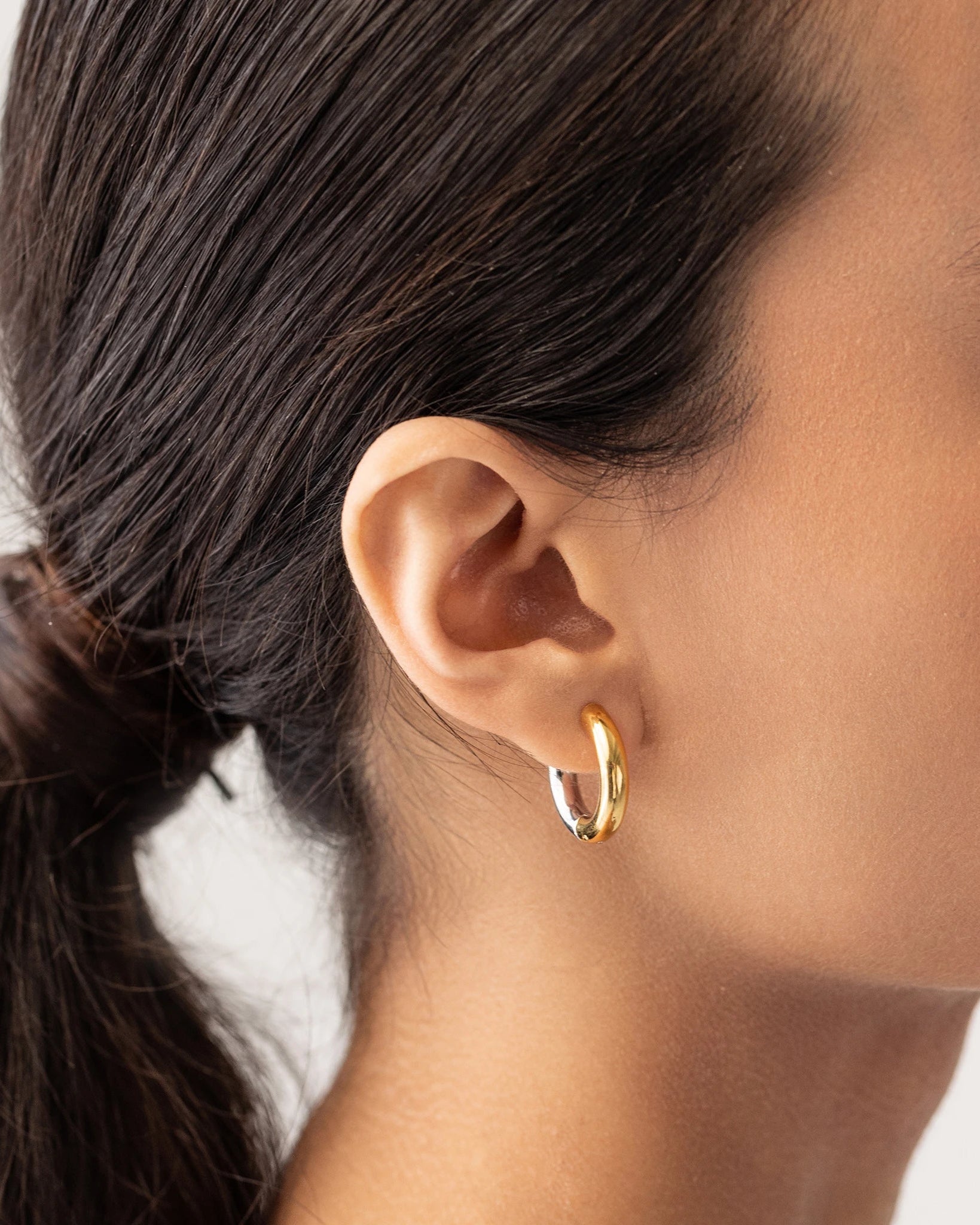 Model wearing the Slim Mix Huggies, a chic pair of two-tone hoop earrings features a combination of gold and silver tones.